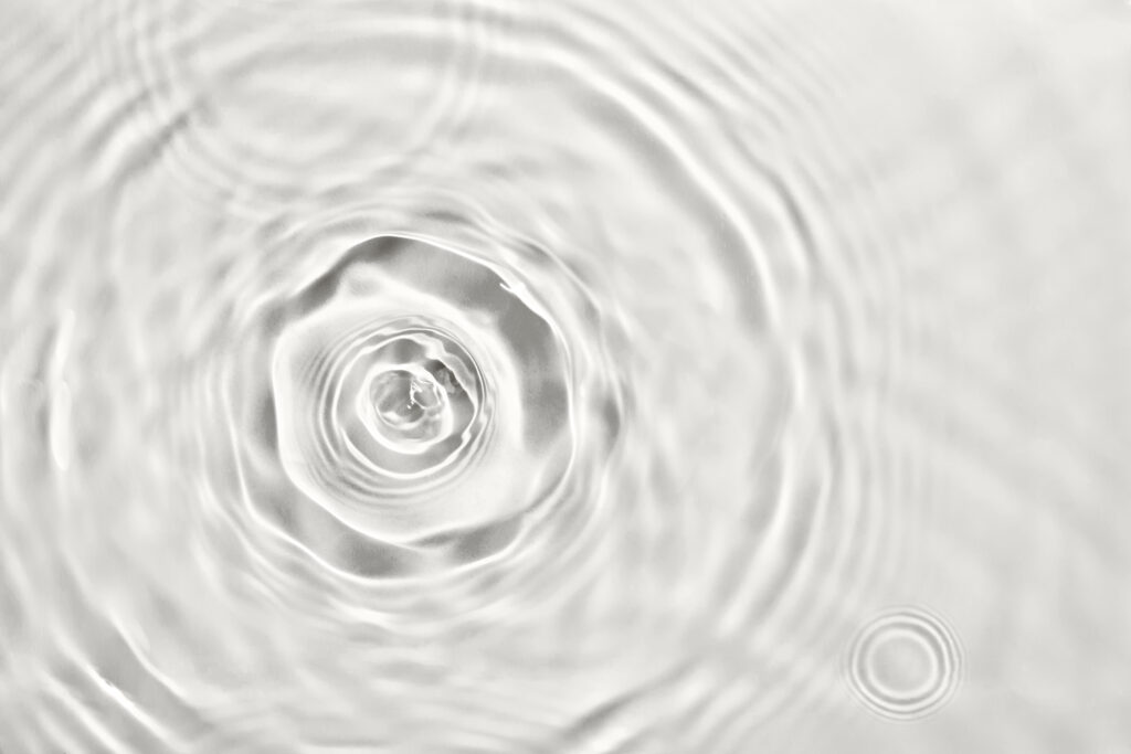 Tropfen trifft Wasseroberfläche und zieht Kreise.